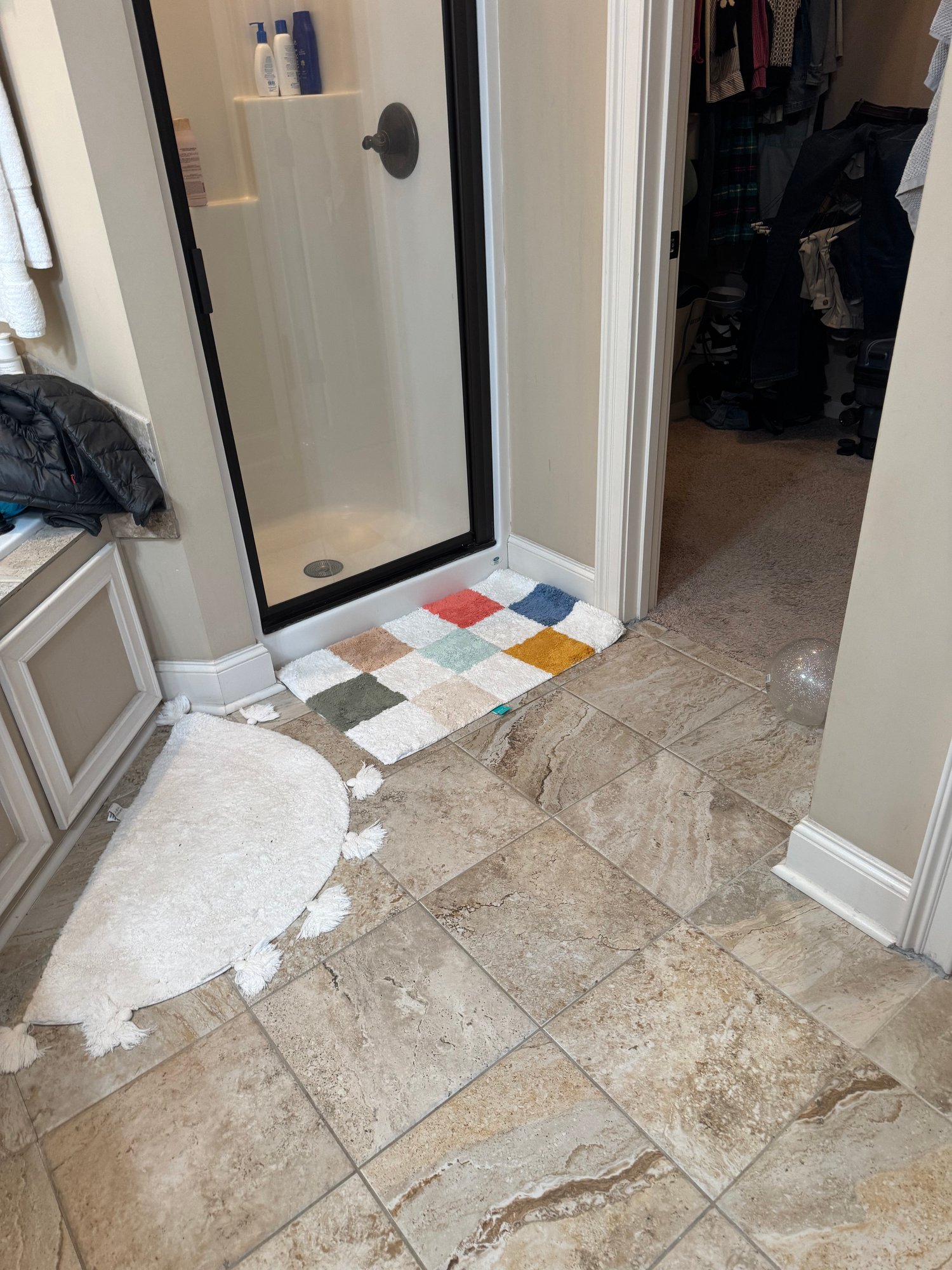 Bathroom with a black-framed shower, beige tile floor, colorful bath mat and an open walk-in closet.