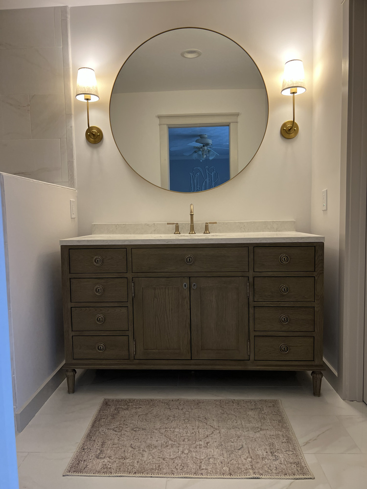 Bathroom vanity remodel in Athens, GA by Encompass Contracting featuring a wood double-sink vanity and round mirror