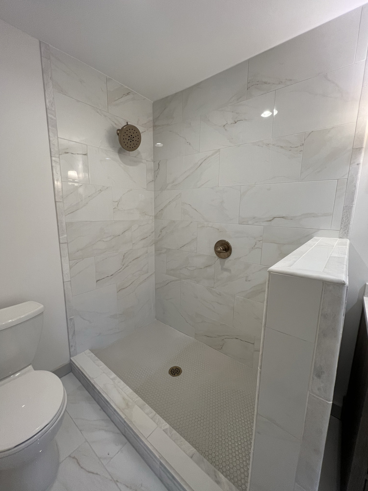 Shower remodel in Statham, Georgia by Encompass Contracting featuring marble tile and brushed gold showerhead