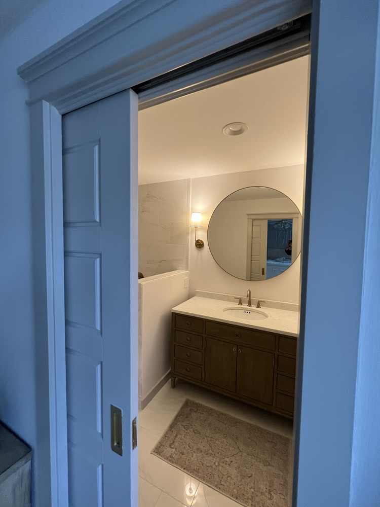 View into a remodeled bathroom in Bishop, GA by Encompass Contracting featuring a round mirror and soft lighting