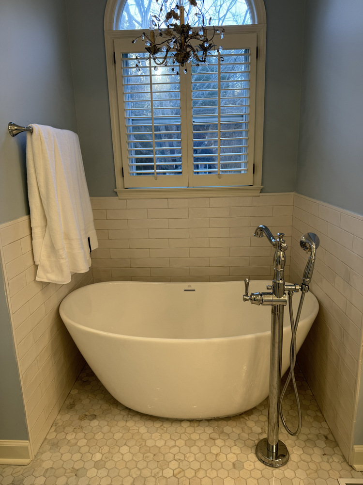 Luxury bathroom renovation in Athens, GA by Encompass Contracting with modern tub and chandelier below arched window