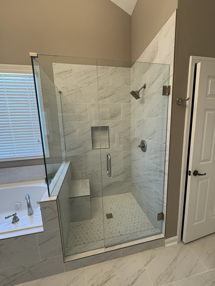 Frameless glass shower remodel in Watkinsville, GA by Encompass Contracting featuring marble-look tile and built-in bench