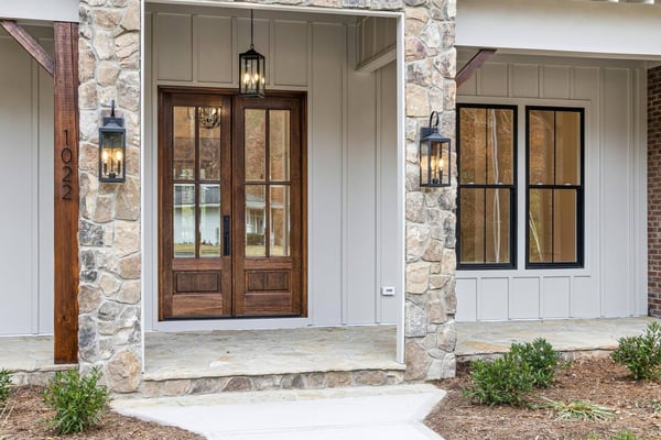 Exterior renovation featuring stone siding, wood double doors, and lantern lighting by Encompass Contracting in Athens, GA - stock